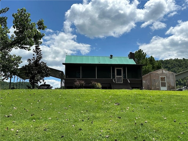 view of front facade with an outbuilding, metal roof, a front lawn, a chimney, and an exterior structure