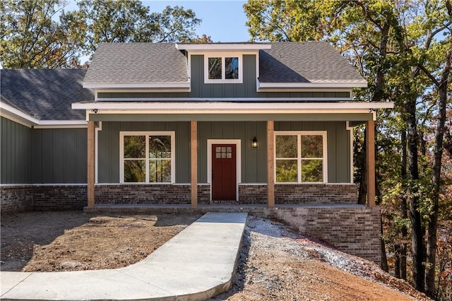 view of front of house with a shingled roof, a porch, board and batten siding, and brick siding