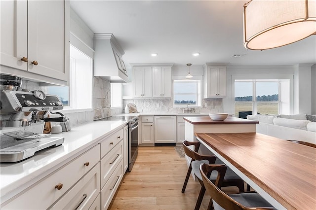 kitchen with decorative light fixtures, light countertops, stainless steel range with electric stovetop, premium range hood, and white cabinetry