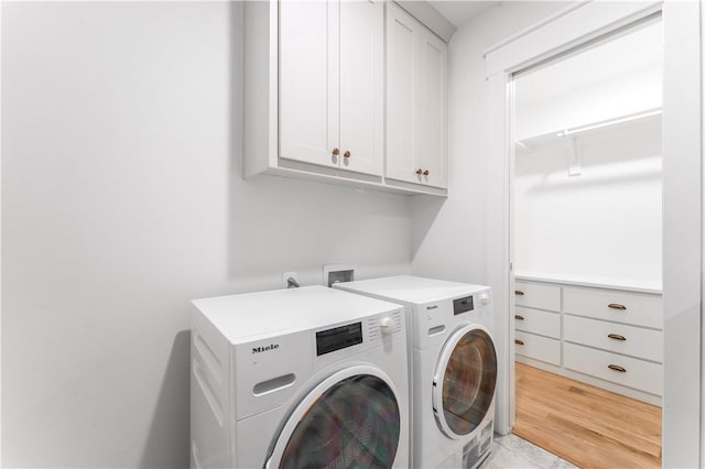 clothes washing area with light wood finished floors, washing machine and dryer, and cabinet space