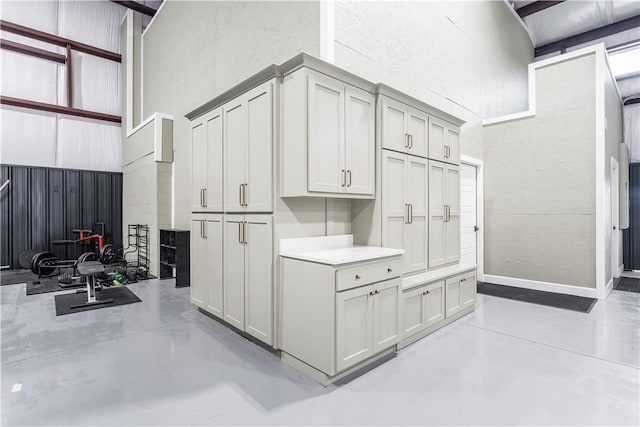 kitchen with a towering ceiling, baseboards, light countertops, and concrete flooring