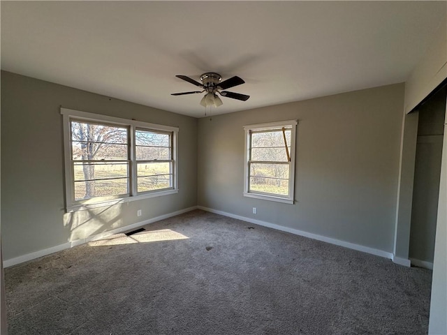 empty room featuring a ceiling fan, carpet flooring, visible vents, and baseboards