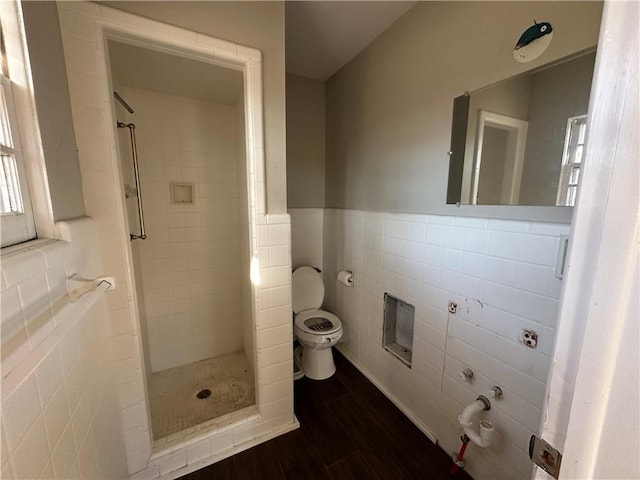 bathroom with tile walls, a shower stall, toilet, and wood finished floors