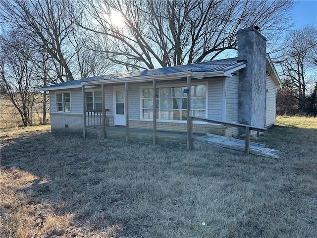 view of front facade with a front yard, covered porch, a chimney, and crawl space