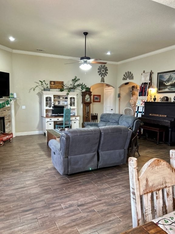 living area featuring a ceiling fan, arched walkways, a fireplace, and dark wood finished floors