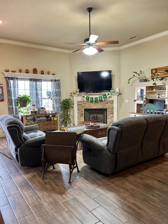 living area featuring visible vents, ceiling fan, ornamental molding, wood tiled floor, and a fireplace