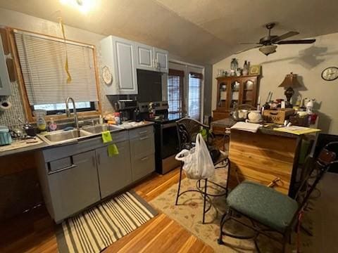 kitchen featuring light wood finished floors, vaulted ceiling, gray cabinets, stainless steel range with electric cooktop, and a sink