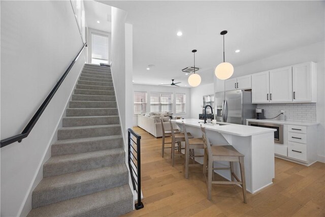 kitchen featuring white cabinetry, open floor plan, light countertops, stainless steel fridge with ice dispenser, and pendant lighting