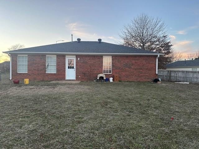 back of property at dusk with brick siding, a lawn, and fence