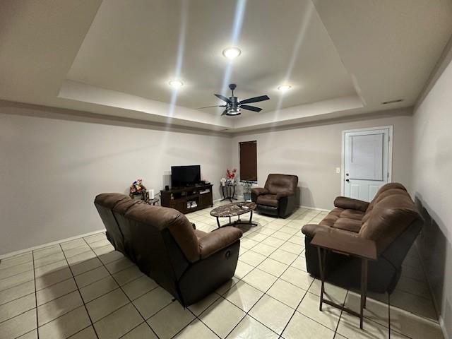 living room with a ceiling fan, a raised ceiling, and light tile patterned floors