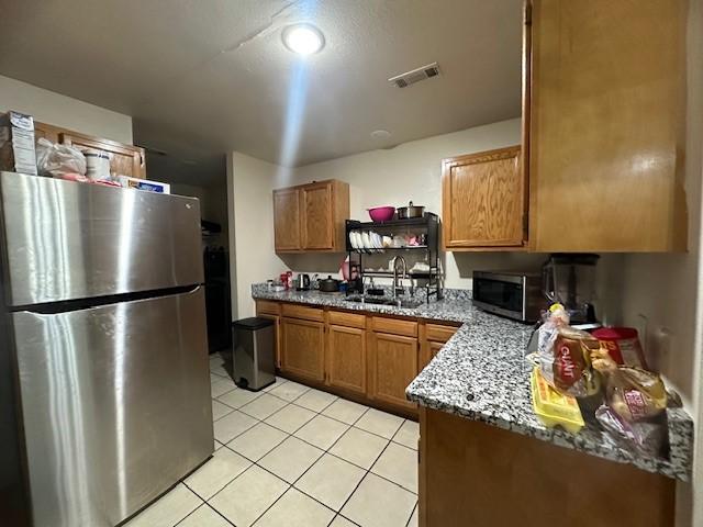 kitchen with light tile patterned floors, visible vents, brown cabinetry, stainless steel appliances, and a sink