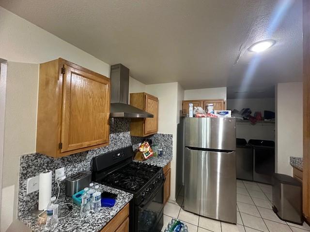 kitchen featuring washing machine and dryer, wall chimney range hood, freestanding refrigerator, tasteful backsplash, and gas stove