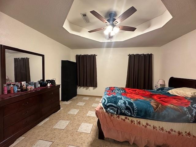 bedroom featuring light tile patterned flooring, a raised ceiling, visible vents, and a ceiling fan