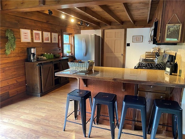 kitchen with a peninsula, a breakfast bar, stainless steel appliances, light wood-style floors, and beamed ceiling