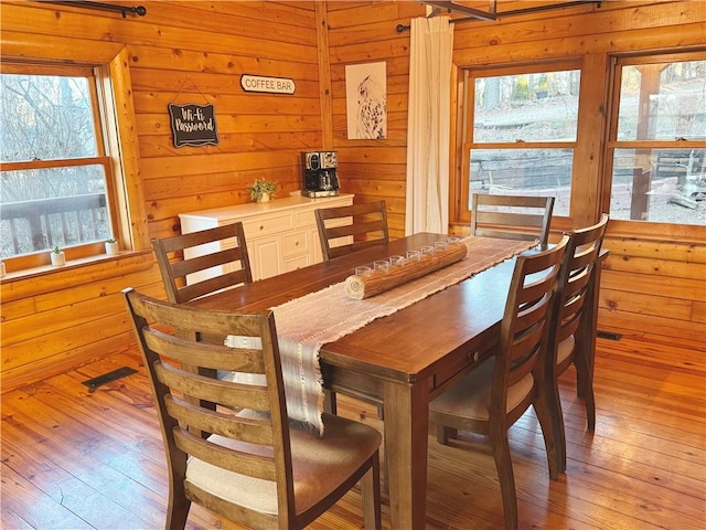 dining space with plenty of natural light, wooden walls, and light wood finished floors