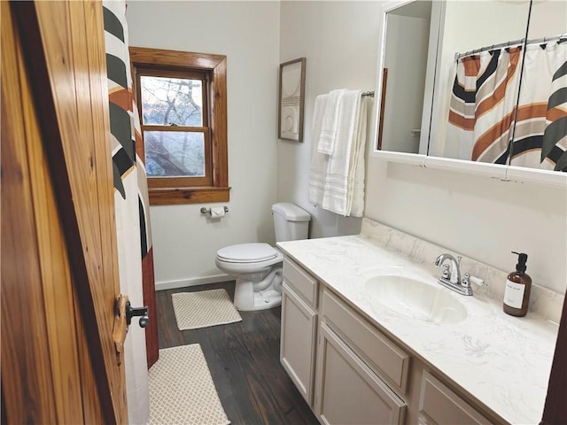 bathroom featuring toilet, baseboards, wood finished floors, and vanity