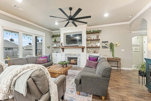 living room with arched walkways, dark wood-style flooring, crown molding, a fireplace, and visible vents