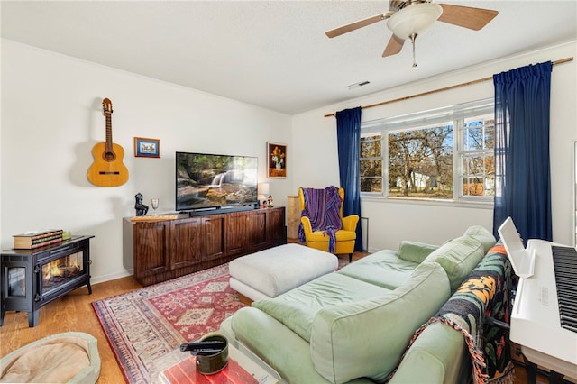 living area featuring ceiling fan, a wood stove, light wood finished floors, and visible vents