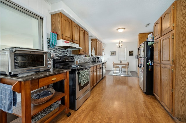 kitchen with a toaster, stainless steel appliances, brown cabinetry, light wood-style floors, and under cabinet range hood