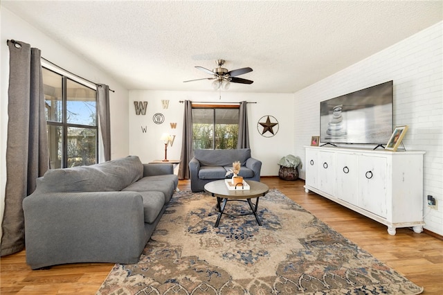 living area featuring a healthy amount of sunlight, a textured ceiling, brick wall, and wood finished floors