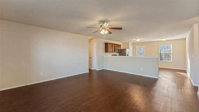 unfurnished living room with dark wood finished floors, a ceiling fan, and baseboards