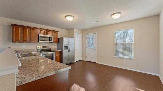 kitchen featuring brown cabinets, dark wood finished floors, appliances with stainless steel finishes, a sink, and baseboards