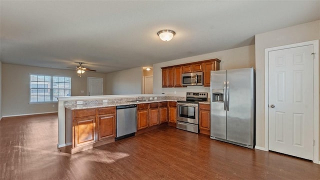 kitchen featuring stainless steel appliances, dark wood-type flooring, a peninsula, a sink, and brown cabinets