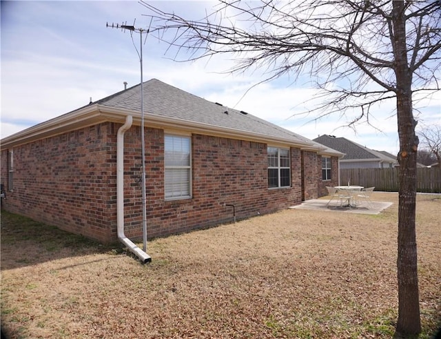 view of side of property featuring a patio area, brick siding, roof with shingles, and fence