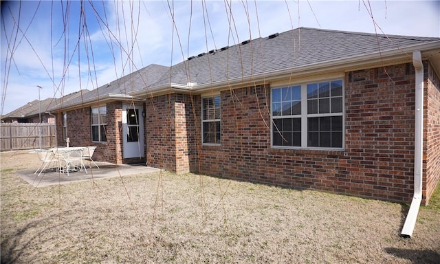 rear view of house with a patio, brick siding, a shingled roof, and fence