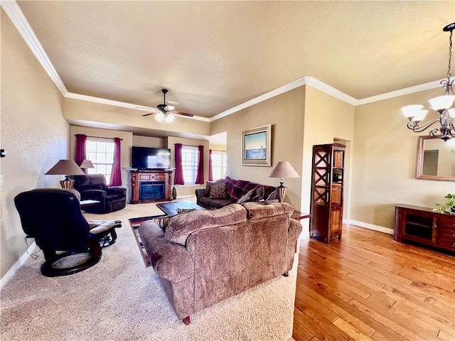 living area featuring baseboards, ornamental molding, light wood-style floors, a glass covered fireplace, and ceiling fan with notable chandelier