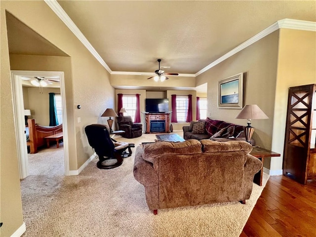 living area with a glass covered fireplace, a ceiling fan, baseboards, and ornamental molding