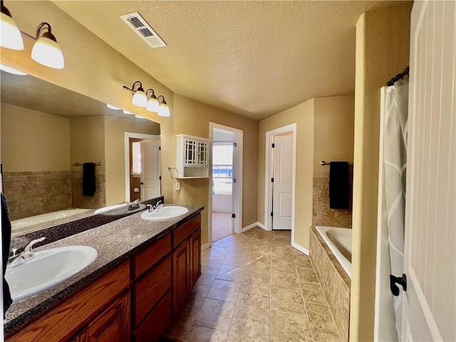 full bath with double vanity, visible vents, a textured ceiling, and a sink