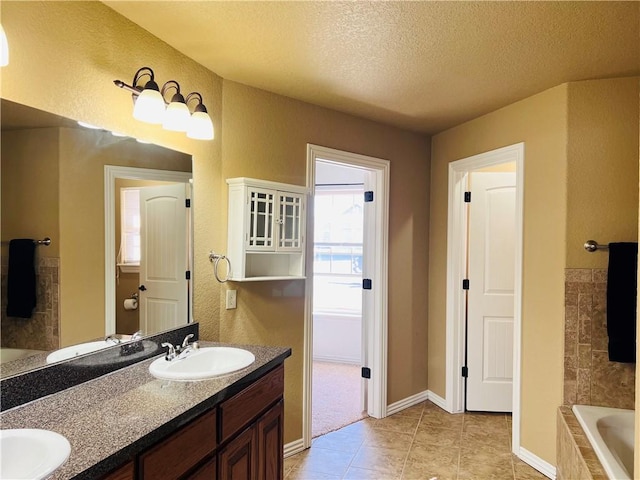 full bathroom featuring tiled bath, tile patterned flooring, a textured ceiling, and a sink