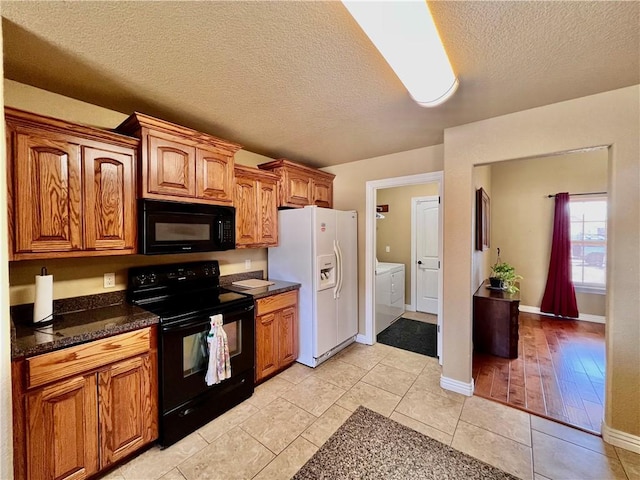 kitchen featuring black appliances, light tile patterned floors, brown cabinetry, a textured ceiling, and separate washer and dryer