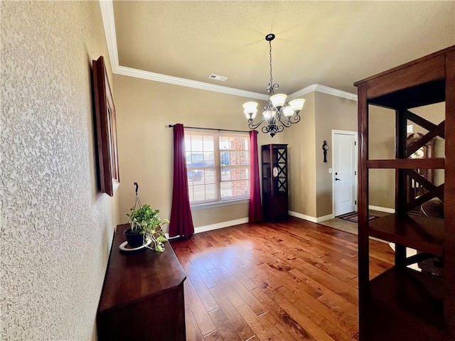 dining space with visible vents, baseboards, ornamental molding, wood finished floors, and a notable chandelier