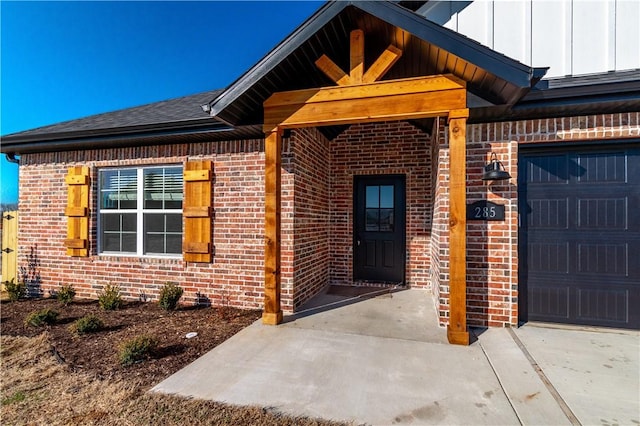 doorway to property with board and batten siding, brick siding, and a garage