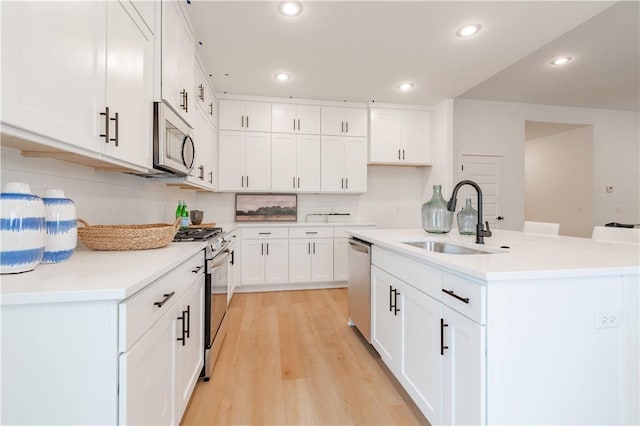 kitchen with a kitchen island with sink, a sink, white cabinetry, light countertops, and appliances with stainless steel finishes