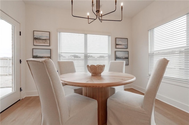 dining area with light wood-style floors, a notable chandelier, baseboards, and a wealth of natural light