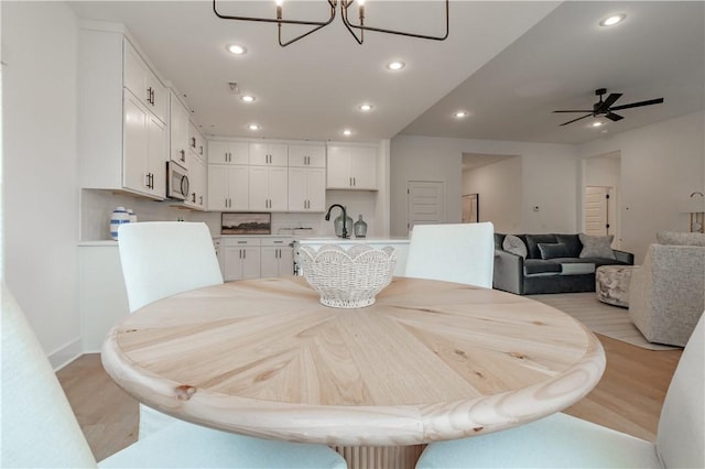 dining space featuring light wood finished floors, ceiling fan with notable chandelier, and recessed lighting