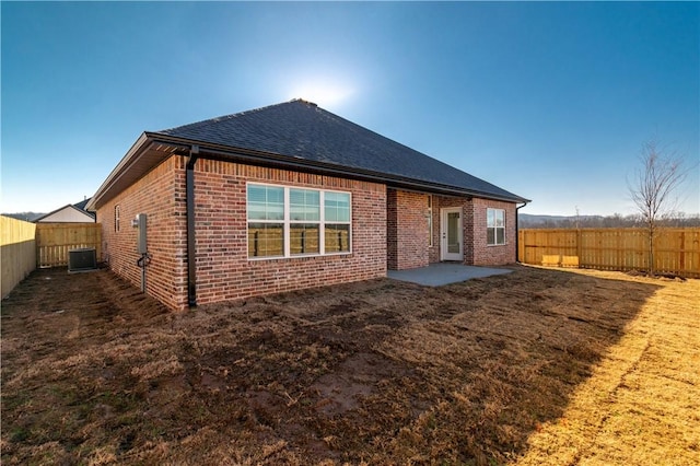 back of house featuring a patio, brick siding, roof with shingles, and a fenced backyard