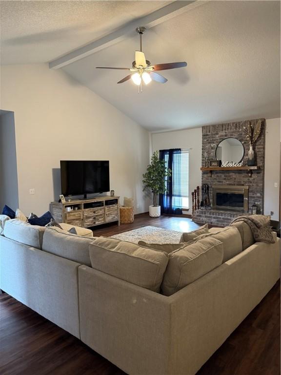 living room featuring dark wood-style floors, vaulted ceiling with beams, a ceiling fan, a brick fireplace, and a textured ceiling