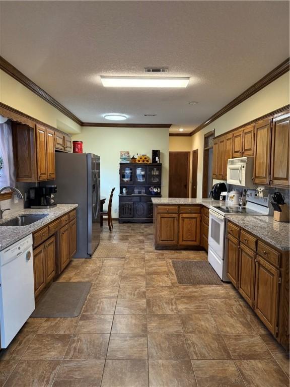 kitchen with a peninsula, white appliances, a sink, visible vents, and ornamental molding