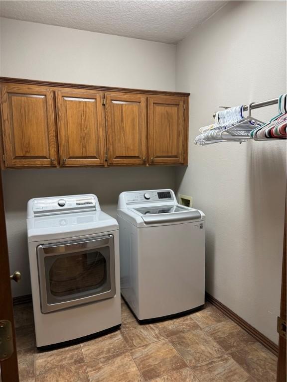 laundry area featuring a textured ceiling, washing machine and dryer, cabinet space, and baseboards