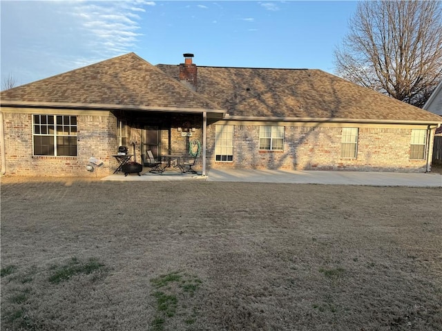 back of property featuring a shingled roof, brick siding, a patio, and a chimney