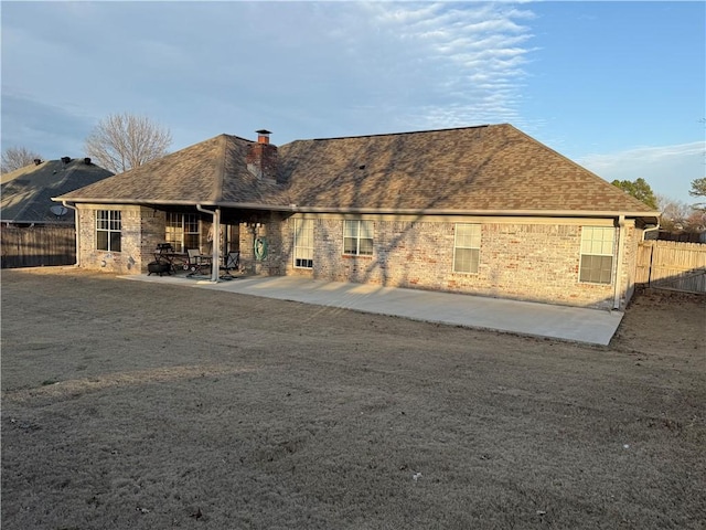 back of property with a shingled roof, a patio area, fence, and a chimney