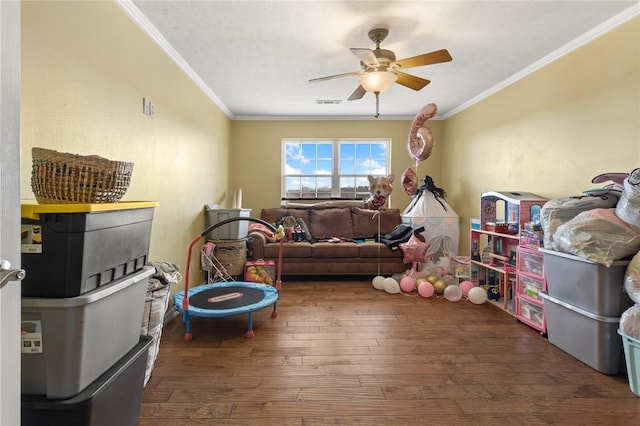 game room featuring ornamental molding, dark wood-style flooring, visible vents, and a ceiling fan