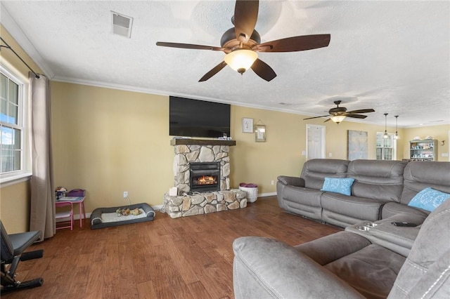 living area featuring a textured ceiling, a fireplace, wood finished floors, visible vents, and ornamental molding