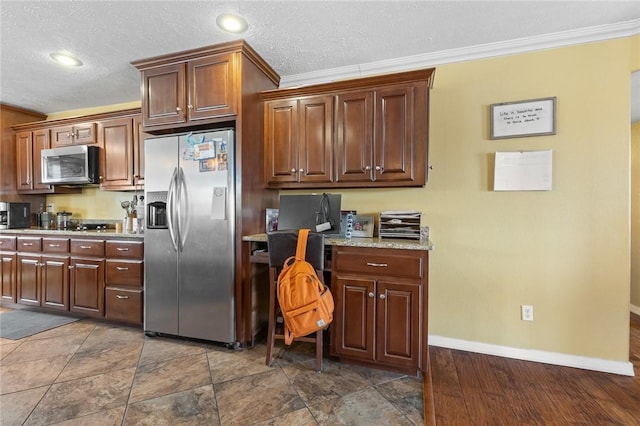 kitchen with crown molding, built in desk, stainless steel appliances, a textured ceiling, and baseboards