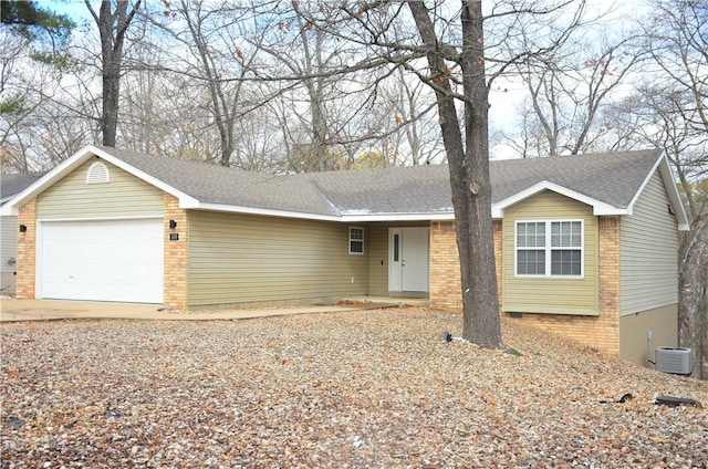 ranch-style house with a garage, brick siding, central air condition unit, and roof with shingles