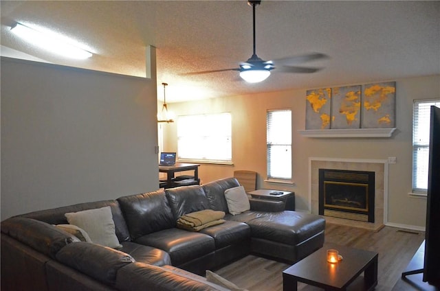 living area with a textured ceiling, wood finished floors, a tile fireplace, and a healthy amount of sunlight